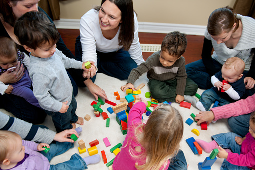 A group of mothers with young children playing with colorful blocks. - Buy credits