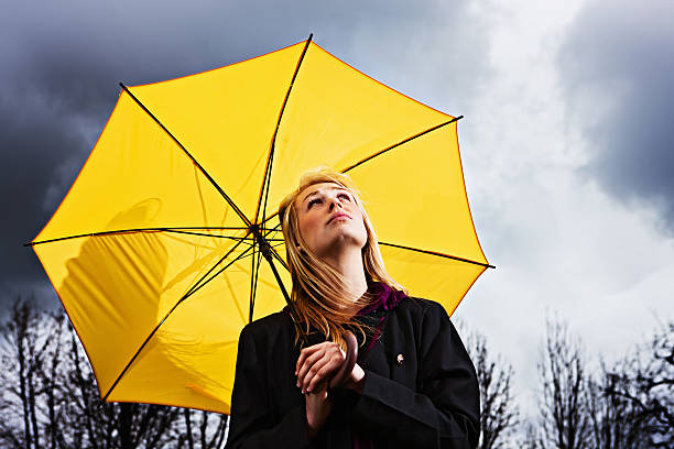 不幸せな若い女性、傘ウェイツにストームに合格 - umbrella women storm yellow ストックフォトと画像