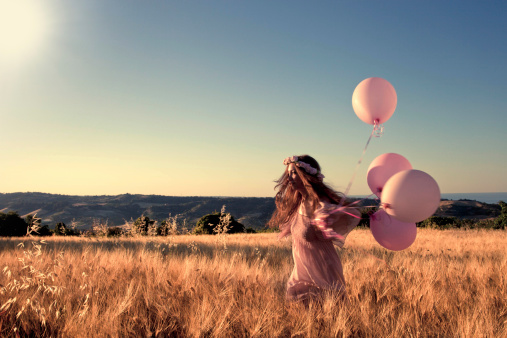 Girl with pink balloons in a cornfield.