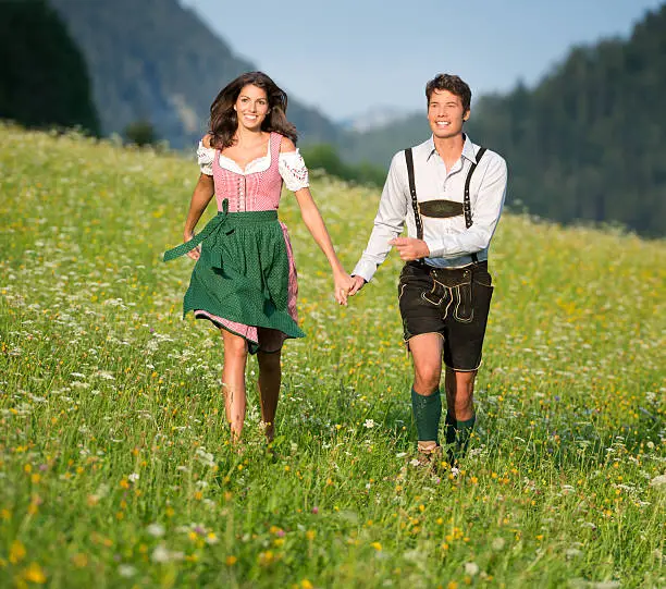 A beautiful couple running through the meadows in traditional Tracht, Dirndl and Lederhosen. Perfect candid shot. Nikon D800e. Converted from RAW.