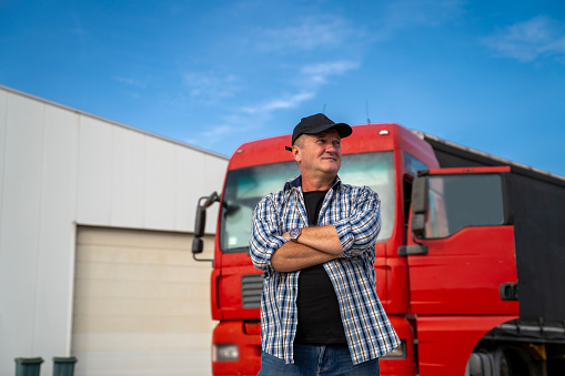 Caucasian man in his fifties with cap and crossed arms standing in front of red truck