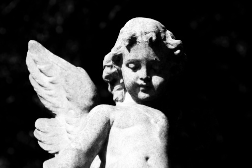 Black and white old statue of little angel - cherub against black background, full frame horizontal composition with copy space
