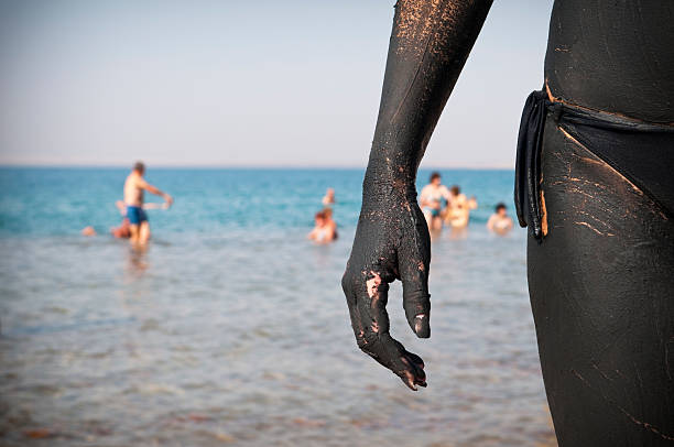 A woman standing by the Dead Sea, her mineral-rich mud coating drying in the sun