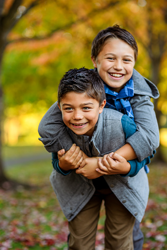 Two multiracial elementary age brothers of Pacific Islander and Caucasian descent playfully embrace and smile at the camera while enjoying time together outside on a beautiful Autumn day.