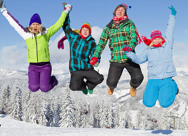 vier jungen menschen in winterkleidung jumping on snow - people group of people friendship salzburg stock-fotos und bilder