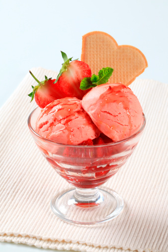 Two bowls of ice cream with strawberry and mango flavors served with pieces of fruit