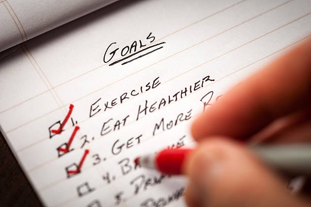 Hand Holding Red Marking Pen Checking Off List of Goals Closeup showing a hand checking off goals that were accomplished. self improvement stock pictures, royalty-free photos & images