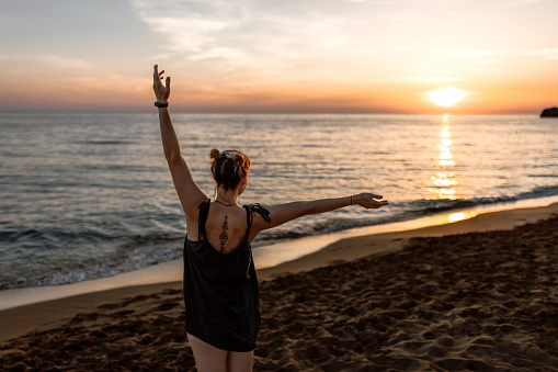 Woman raising arms while watching beautiful sunset at beach