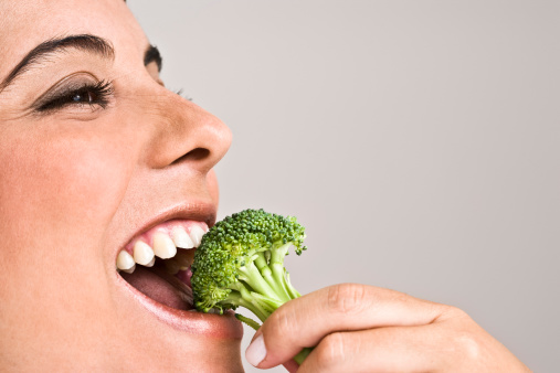 Close up of woman eating broccoli, smiling, portrait