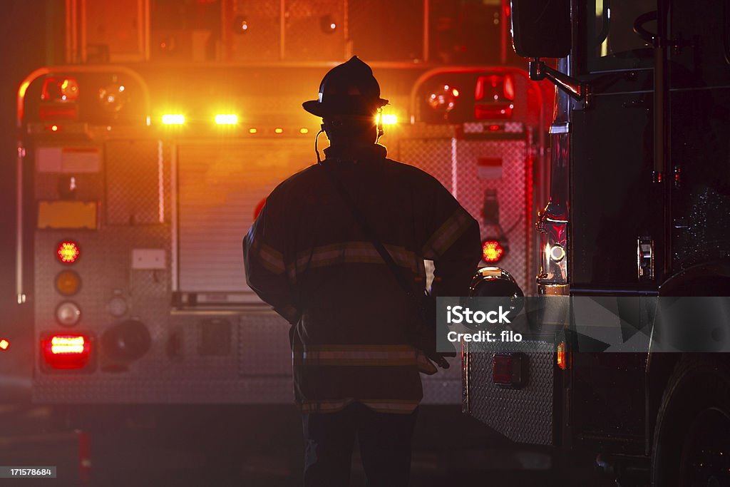 Firefighter Firefighter silhouetted against a fire truck with flashing lights at an emergency scene. Firefighter Stock Photo