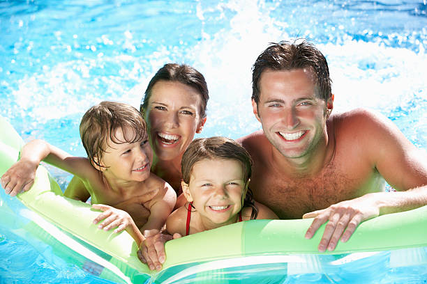 Family On Holiday In Swimming Pool Family On Holiday In Swimming Pool Smiling To Camera. one piece swimsuit photos stock pictures, royalty-free photos & images