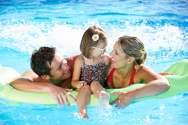 A family having fun in the swimming pool Family On Holiday In Swimming Pool Smiling And Laughing. one piece swimsuit photos stock pictures, royalty-free photos & images