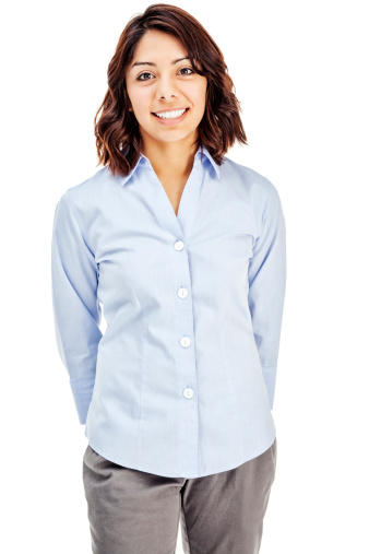 Photo of an attractive young Hispanic businesswoman in blue button-down shirt, standing with hands behind her back; isolated on white.