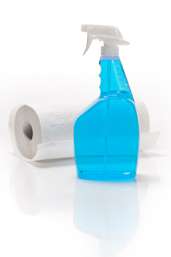 Bottle of blue window cleaning product with a roll of paper towels on white background