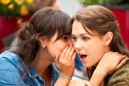 Young Woman Whispering Secret in Another Woman's Ear at Cafe