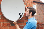 Man Fitting TV Satellite Dish To House Wall
