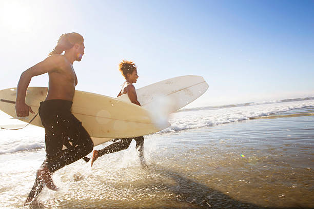 surfeurs sur la plage - horizontal men women surfboard photos et images de collection