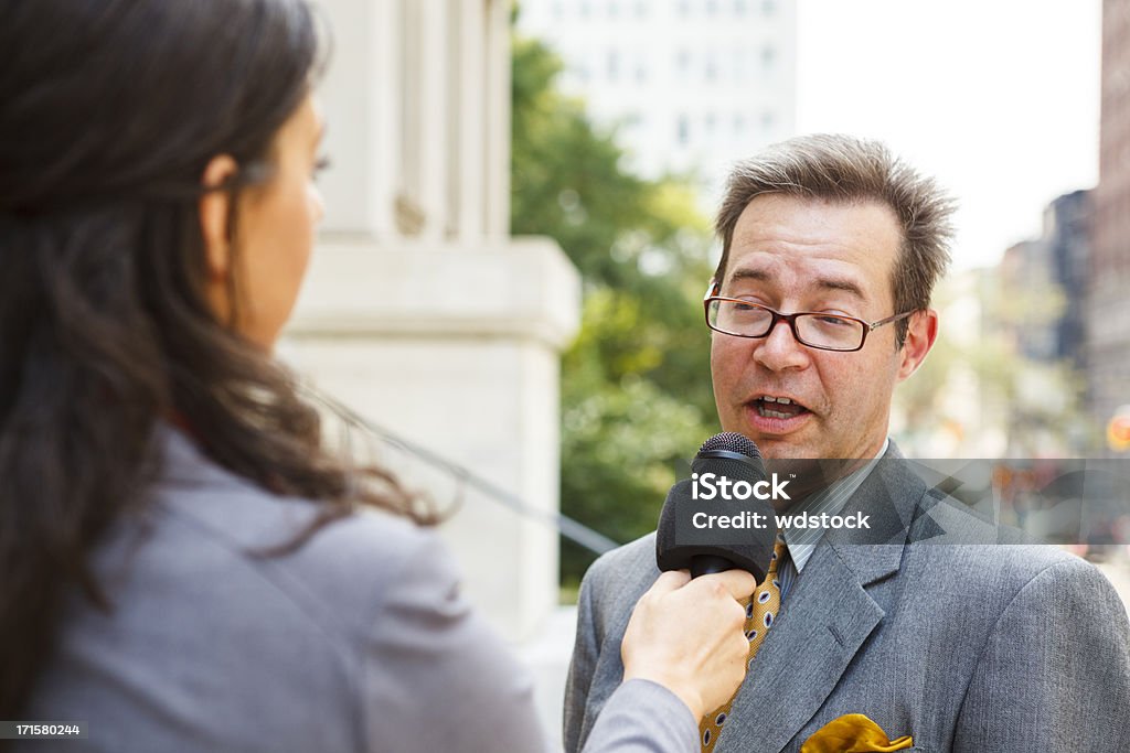 Woman Interviews Man A smiling well dressed man being interviewed by a woman with a microphone. Interview - Event Stock Photo