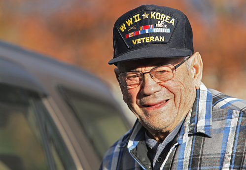 World War II and Korean War veteran. Proud military veteran senior man. 90 years old. Standing next to car he drives almost every day. Smiling autumn portrait natural evening light.