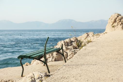 green broken empty bench on concrete floor against mediterranean ocean