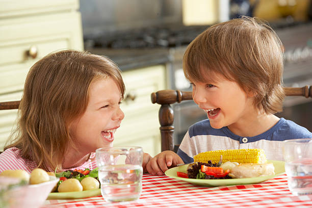 Boy And Girl Eating Meal In Kitchen Smiling And Laughing.