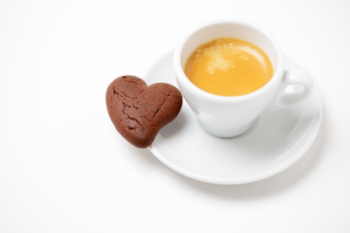 A fresh cup of espresso coffee with a heart-shaped chocolate flavoured biscuit, on a white background with copy space.