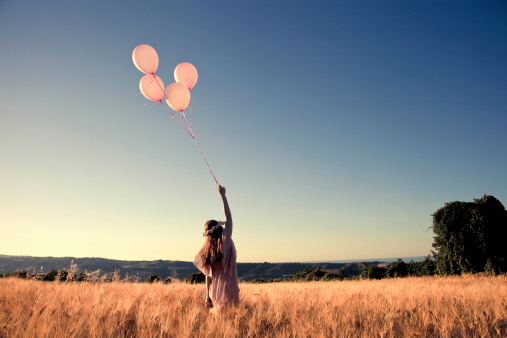 Girl with pink balloons in a cornfield.