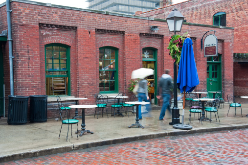 Unrecognizable couple walking in the rain  past a cafe  in the historical Distillery District in Toronto.