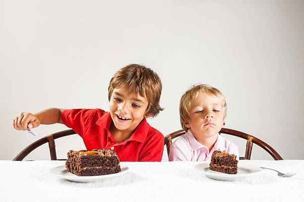 Big piece of cake and a little one, inequality concept. A conceptual photograph depicting inequality between two brothers, one with a very large slice of chocolate cake and the other with a small slice.Please browse: unfairness photos stock pictures, royalty-free photos & images