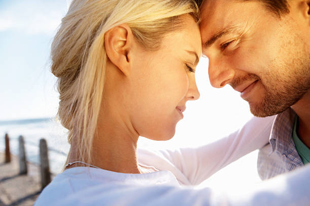 Epic close up portrait of a adorable european female with sunglases black eyes loolking into camera smiling while is kissded by her man against beautiful sunset with sunflares .