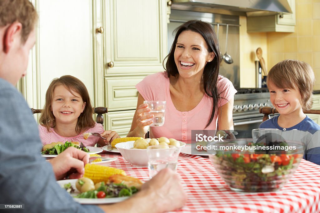 A happy family sharing a meal in the kitchen Family Eating Meal Together In Kitchen Smiling And Laughing. Eating Stock Photo