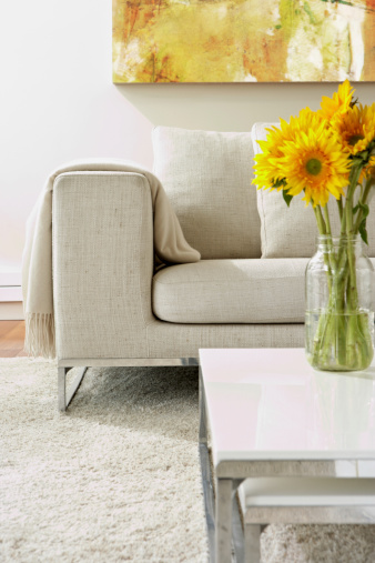Empty modern living room with white rug and a vase with sunflowers arrangement on a coffee table.  Vertical composition.