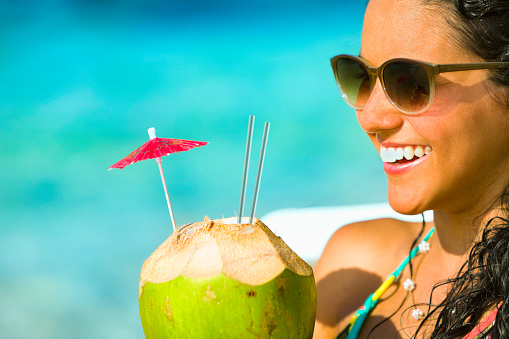 Close-up of a happy young woman with coconut drink in tropical turquoise beach