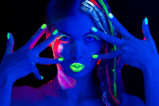 Young women portrait in Ultraviolet Light with Lime Green Eyelashes, lips, Fingernails ,Multi Colored Hair and Makeup. With neon lenses.