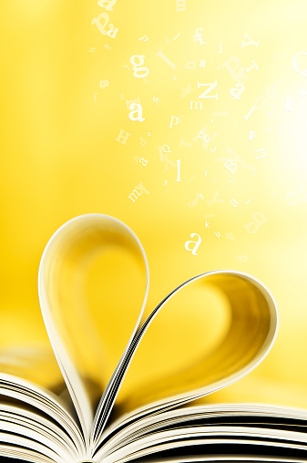Book pages curled into heart shape, flying letters on the yellow background.