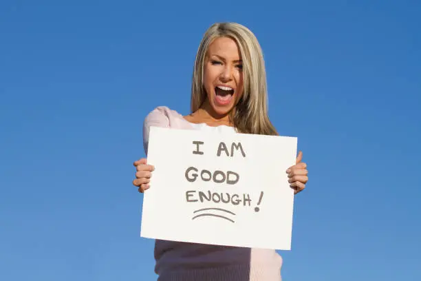 happy young adult holding sign that says "i am good enough" as a confidence and self esteem concept
