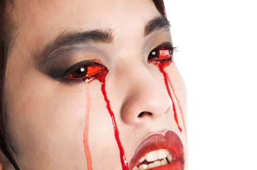 Horizontal studio shot on white of Asian vampire crying blood, looking at camera.
