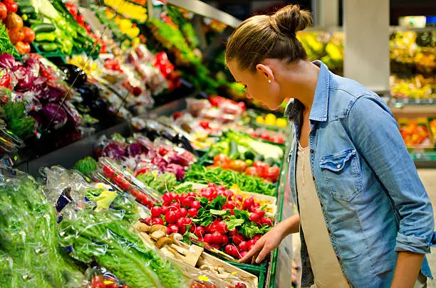 Photo of A young woman looking at fresh vegetables in the supermarket