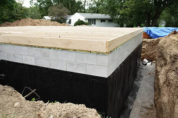 A suburban residential construction home addition has a new basement foundation with a durable, heavy-duty plastic basement waterproofing shroud newly installed..