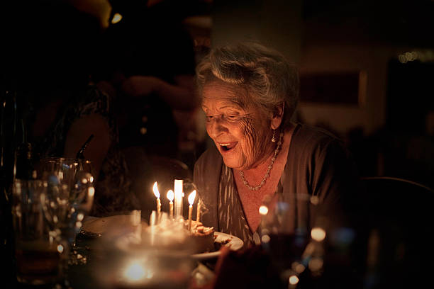 Elderly Lady:  Birthday Celebration Happy 85 year old woman ready to blow out birthday candles.  High level of noise, due to low light.More senior lady lifestyle shots: woman birthday cake stock pictures, royalty-free photos & images