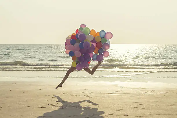 jumping girl with balloons at sea beach