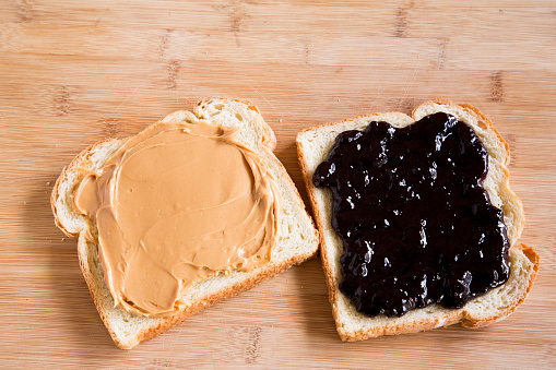 Simple peanut butter and jelly sandwich with strawberry jam and chunky peanut butter on white bread, separated and placed on a bamboo cutting board with soft natural window light.