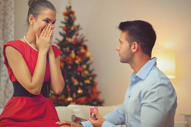 A man proposing to a woman in a red dress at Christmas stock photo