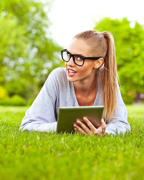 jeune femme avec une tablette dans un parc - women grass glasses e reader photos et images de collection