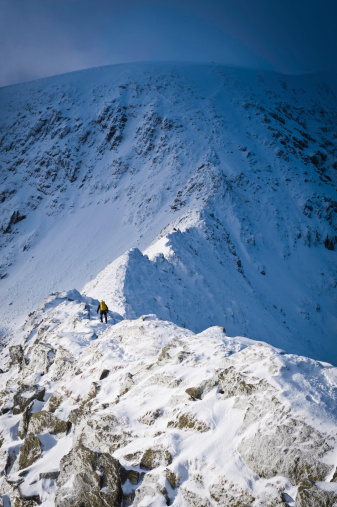 Mountaineer climbing along the famous dramatic mountain ridge covered in full winter snows to the summit of Helvellyn above, Lake District National Park, Cumbria, UK. ProPhoto RGB profile for maximum color fidelity and gamut.