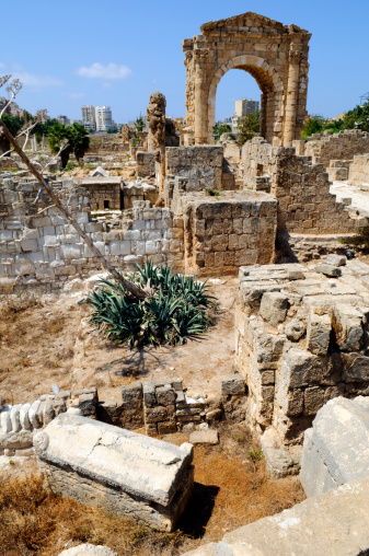 Roman ruins at the Al-Bass Archaeological Site in Tyre, Lebanon. Towering in the background is the monumental archway, built in the second century AD. In the foreground is a sarcophagi. Modern buildings are in the far distance.