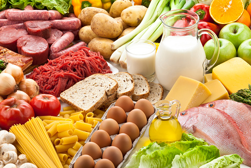 A large group of food.  The assortment includes fruits, vegetables, meat, fish and dairy products.  The food is mostly sorted by type.  The dairy products are in the center, while the rest of the food is circled around the dairy products. Studio photo taken with DSRL Canon EOS 5D Mk II