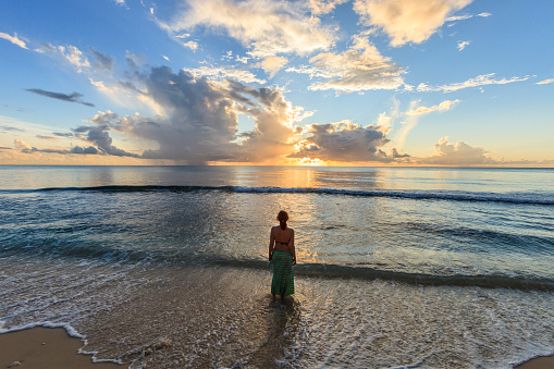 Woman standing on the beach of Paynes Bay at sunset. Surrounded by a beautiful stretch of sand, this is one of the most popular beach on the west coast of Barbados. 