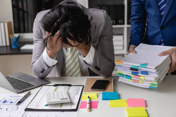istock Young Asian accountant, office worker working with documents, tired and stressed, hands covering face, sitting at table in office with coworkers bringing documents. 1715898321