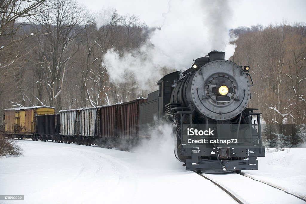 Steam Locomotive Pulling Train in Winter Snow, Rounding Curve Steam locomotive pulling freight train rounding curve in winter snow pushing smoke, historical reenactment near Cumberland, Maryland, MD, USA. Steam Train Stock Photo
